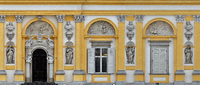  Fragment elewacji pałacu od strony zachodniej. Żółta elewacja, płaskorzeźby nad oknami, pomiędzy nimi rzeźby, po lewej drzwi z dekoracyjnym portalem